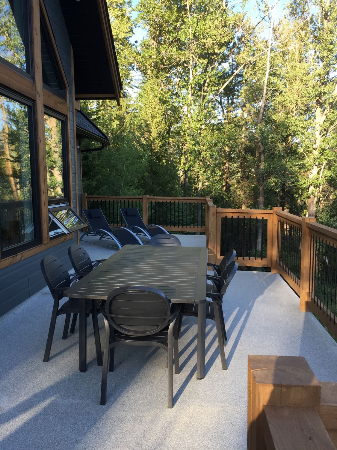 Outdoor dining table for six on the deck, sun loungers at the far end among the trees