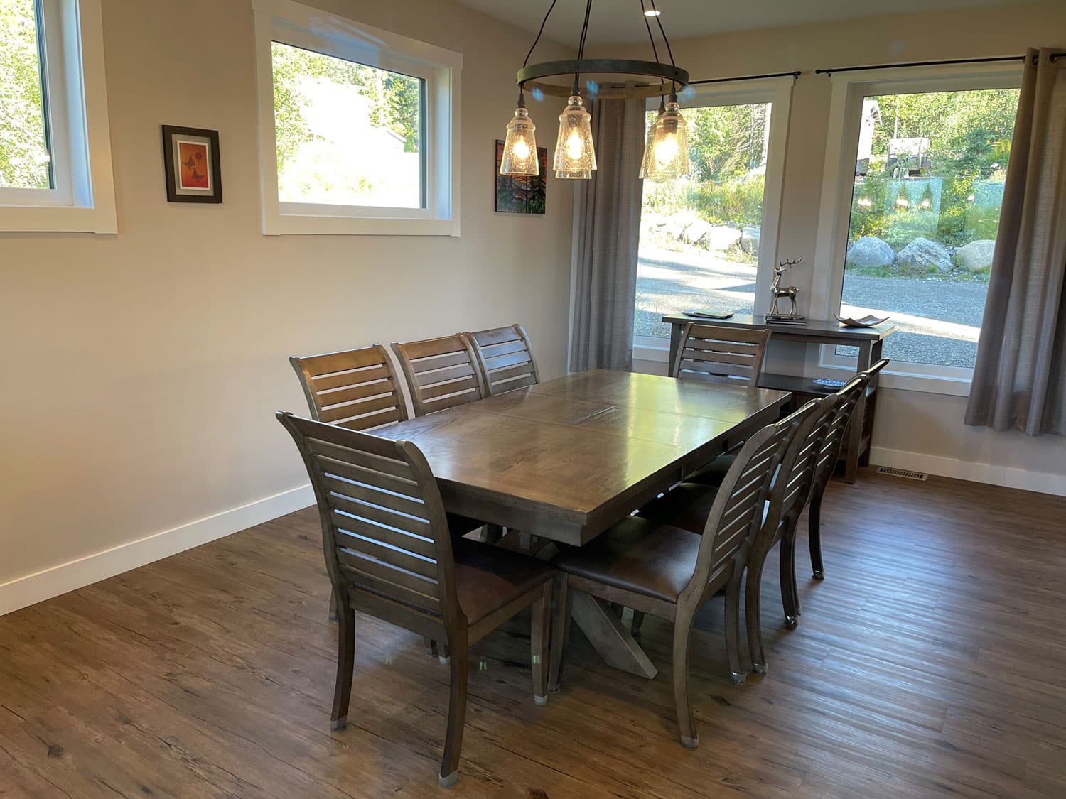 Dining table seating eight under a wagon-wheel pendant light, with windows on two sides