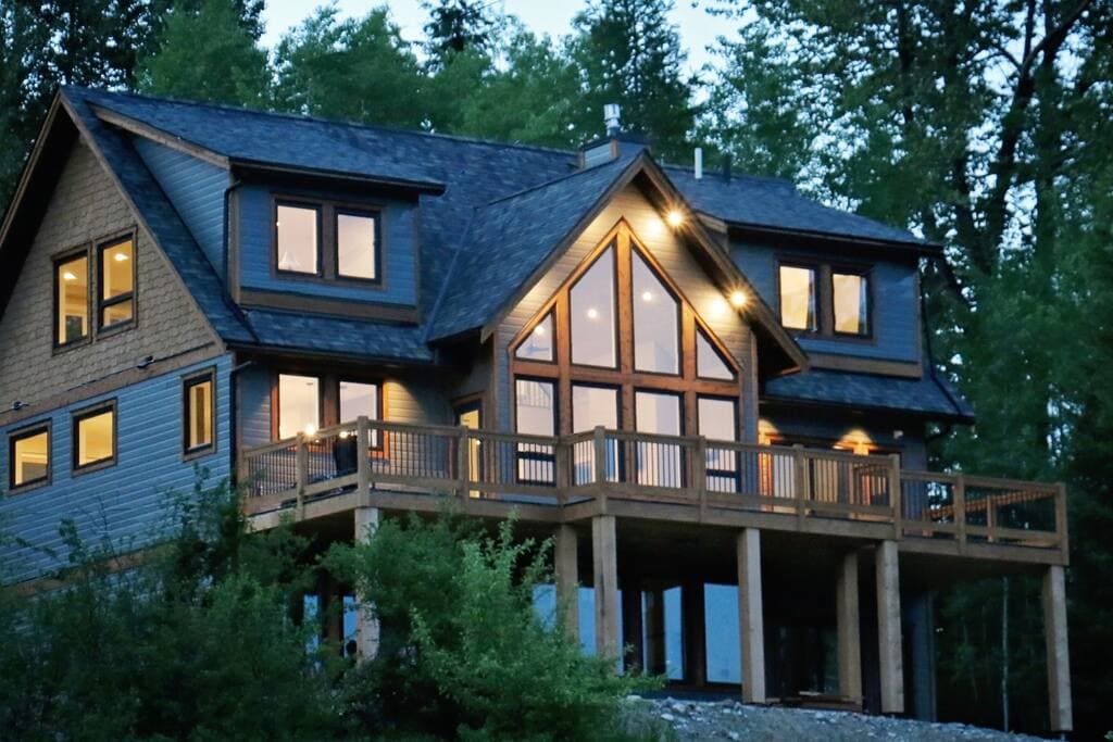 The Perch at dusk, its tall gable windows glowing warm above the wraparound deck, framed by trees