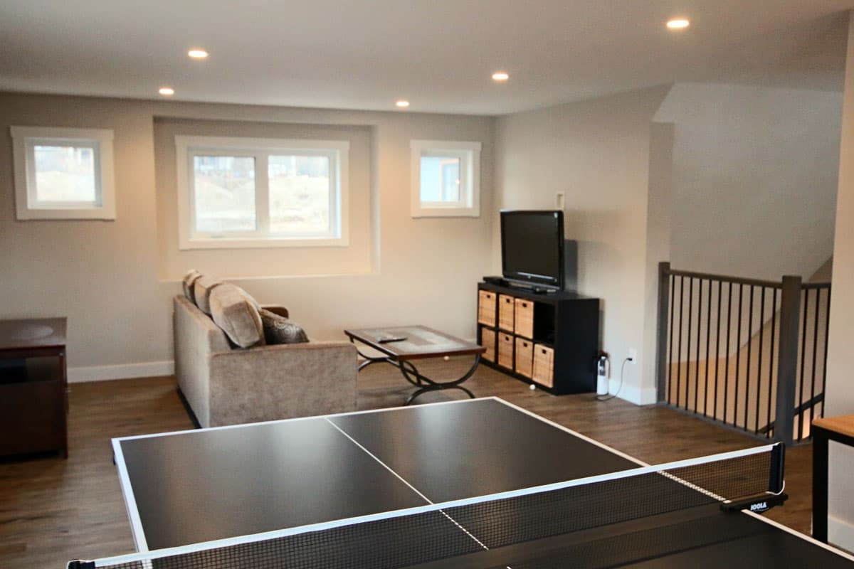 Games loft seen across the table tennis net, with the sofa, TV and stairwell railing beyond