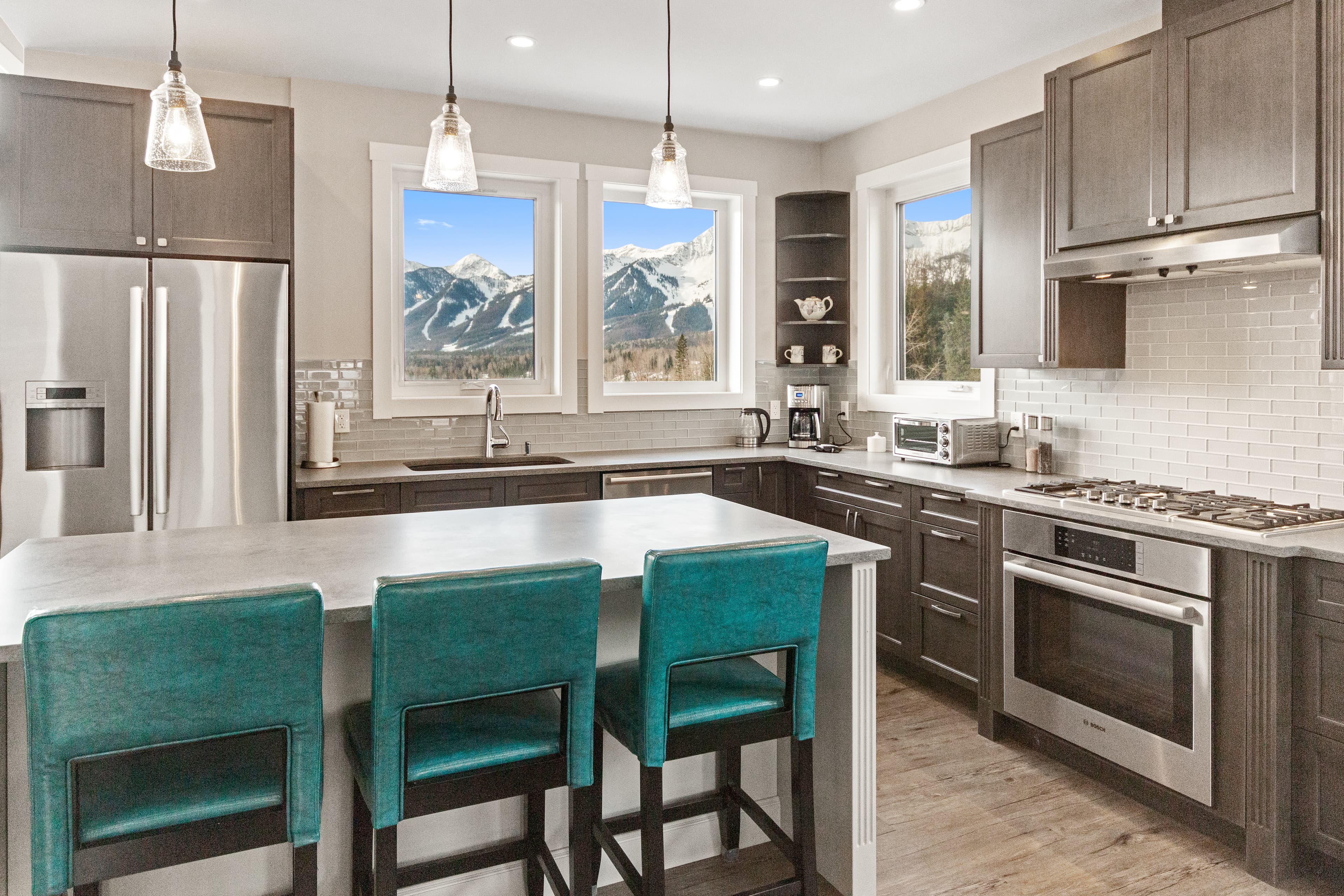 Kitchen with gas range, stainless appliances and island seating for three, the ski hill visible through the windows over the sink