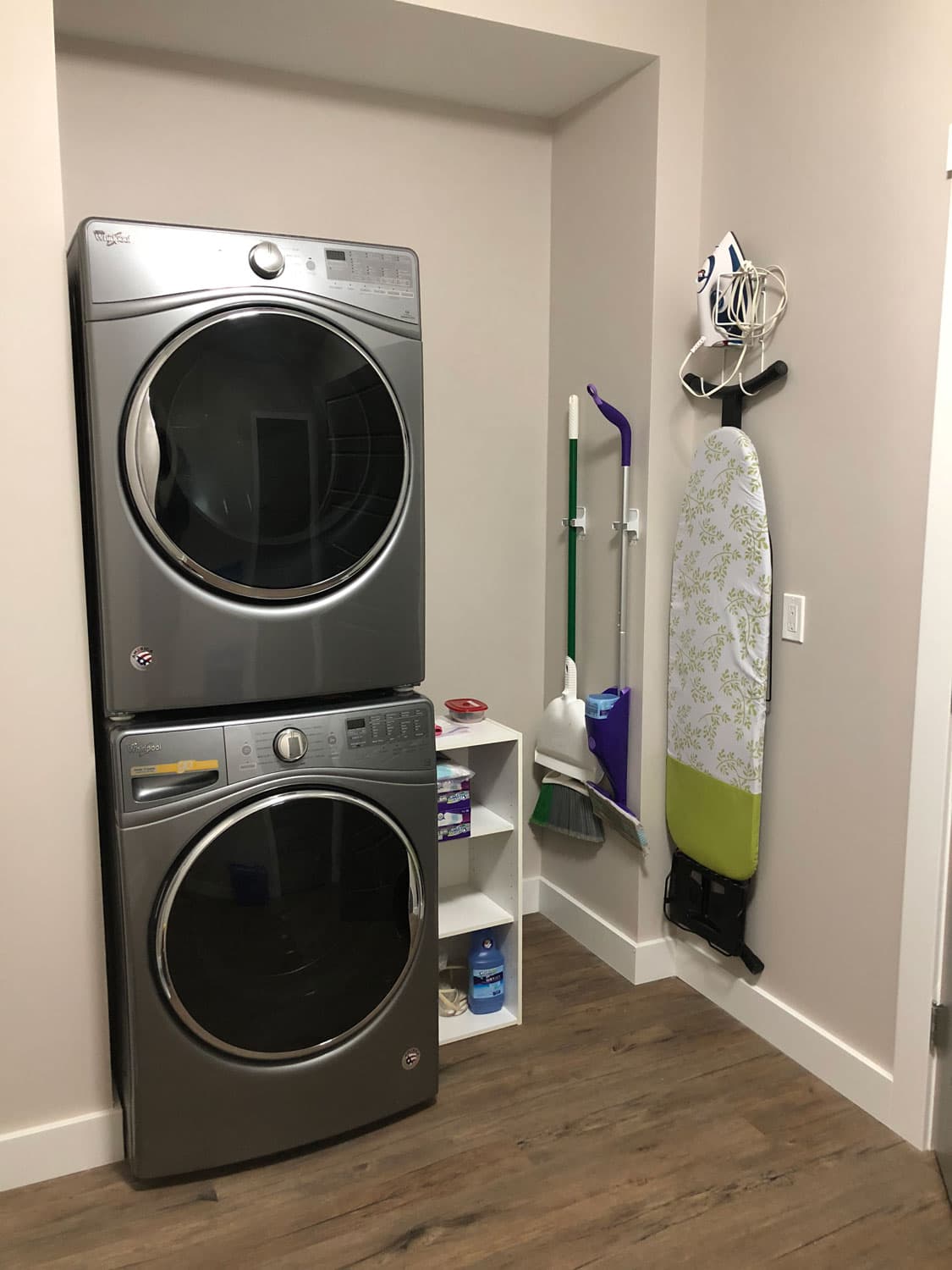Laundry room with stacked front-loading washer and dryer, ironing board and cleaning kit