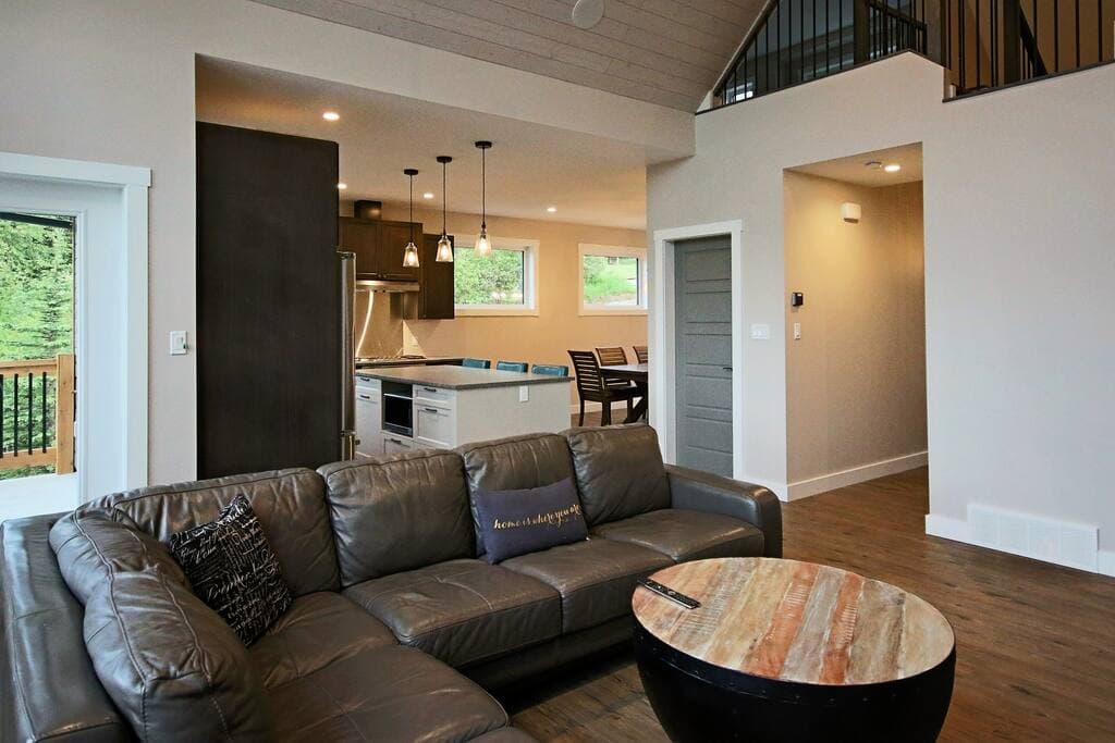 Open-concept main floor: leather sectional and round coffee table, with the kitchen island and dining area beyond and the loft railing above