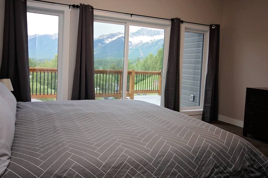 View from the primary bedroom's king bed through the deck doors to the mountains above Fernie